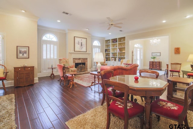 dining room with dark wood-style flooring, visible vents, baseboards, ornamental molding, and a brick fireplace