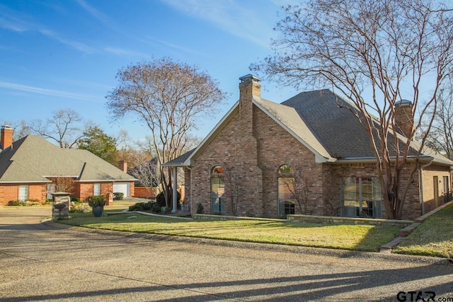 view of home's exterior with a yard, brick siding, and a chimney