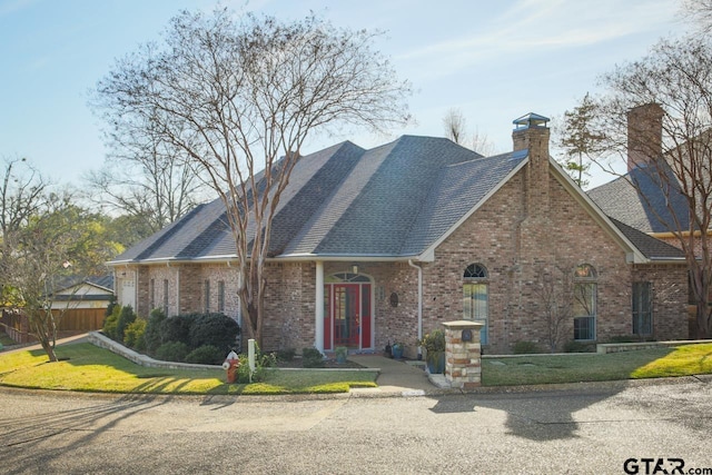 view of front of property featuring a front yard, brick siding, a chimney, and roof with shingles