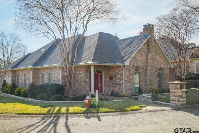 view of front facade featuring brick siding, a chimney, a front lawn, and roof with shingles