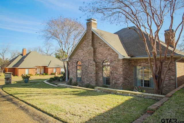 view of front of property featuring roof with shingles, brick siding, a chimney, and a front lawn