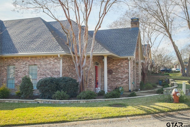 view of front facade featuring a front yard, roof with shingles, a chimney, and brick siding