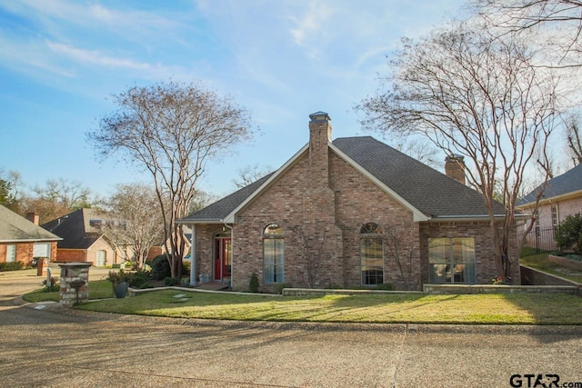 traditional-style home featuring brick siding, a shingled roof, fence, a chimney, and a front yard