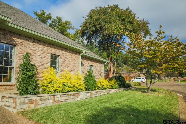 view of side of home with brick siding, roof with shingles, and a yard