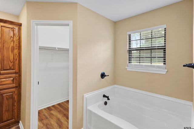 bathroom featuring a spacious closet, wood finished floors, and a bath