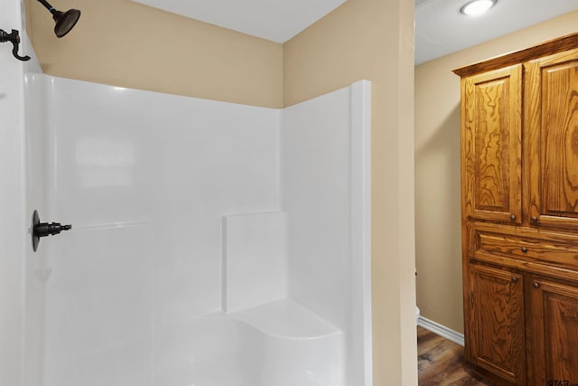 bathroom featuring baseboards, toilet, a shower, and wood finished floors