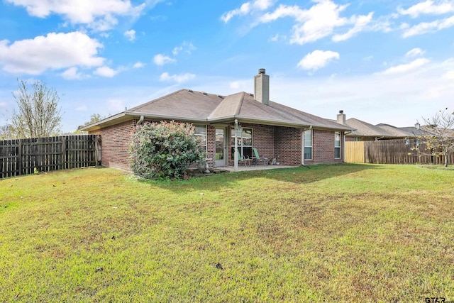 rear view of property featuring a yard, a fenced backyard, brick siding, and a chimney