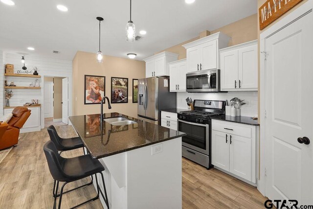 17127 Meadowview Ln, Lindale, TX 75771 - kitchen featuring appliances with stainless steel finishes, white cabinets, a kitchen bar, an island with sink, and light wood-type flooring