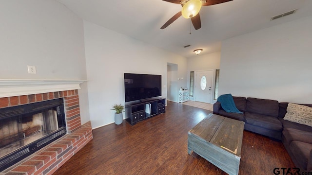 living room featuring a brick fireplace, dark wood-type flooring, and ceiling fan