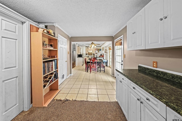 kitchen featuring dark stone counters, light tile patterned flooring, crown molding, ceiling fan, and white cabinetry