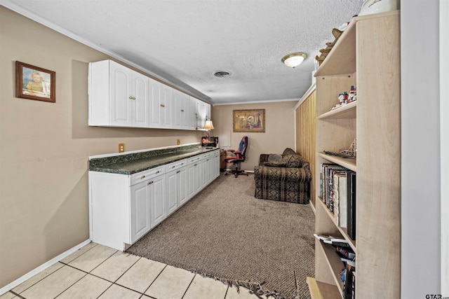 kitchen featuring a textured ceiling, light colored carpet, crown molding, and white cabinets