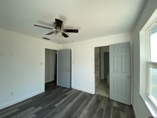 unfurnished bedroom featuring ceiling fan, ensuite bathroom, dark hardwood / wood-style floors, and multiple windows