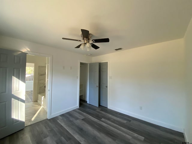 unfurnished bedroom featuring ensuite bath, dark wood-type flooring, and ceiling fan