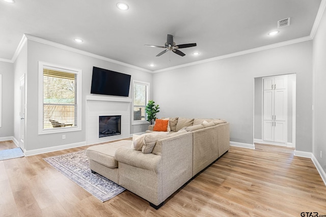 living area featuring crown molding, recessed lighting, light wood-style floors, a glass covered fireplace, and baseboards