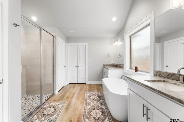 bathroom with a stall shower, two vanities, a sink, and a soaking tub