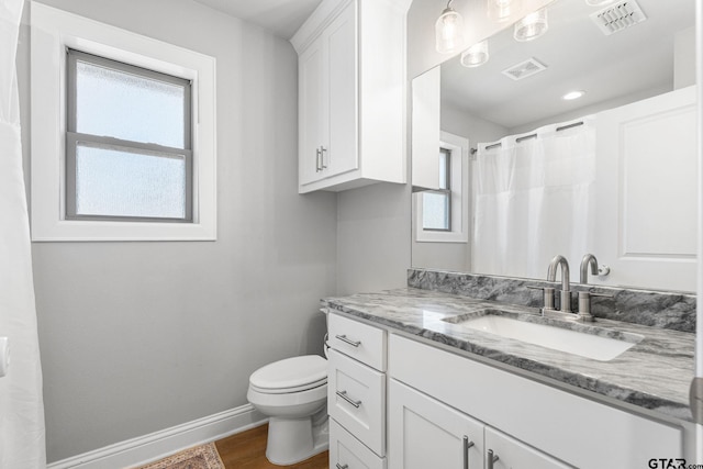 full bath featuring toilet, vanity, visible vents, and baseboards