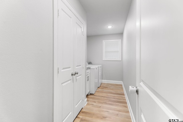 clothes washing area with washing machine and dryer, laundry area, baseboards, and light wood finished floors