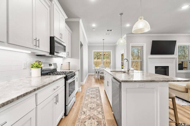 kitchen with open floor plan, a sink, stainless steel appliances, light wood-type flooring, and backsplash