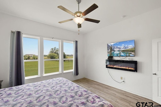 bedroom featuring baseboards, wood finished floors, a ceiling fan, and a glass covered fireplace