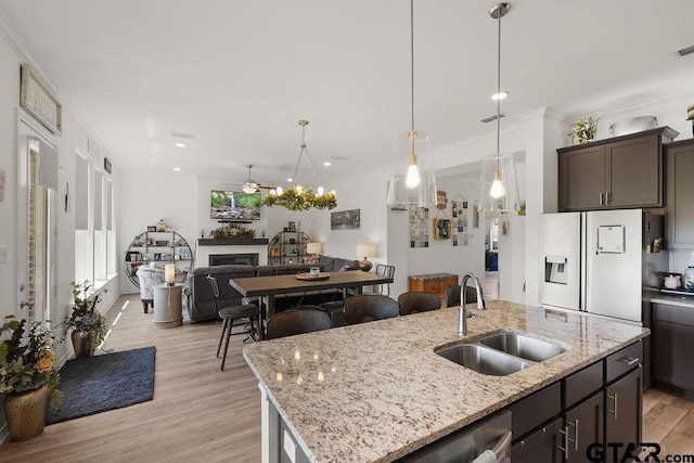 kitchen featuring a kitchen island with sink, a sink, a fireplace, white refrigerator with ice dispenser, and open floor plan