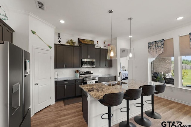 kitchen featuring a sink, appliances with stainless steel finishes, light wood-style floors, light stone countertops, and ornamental molding