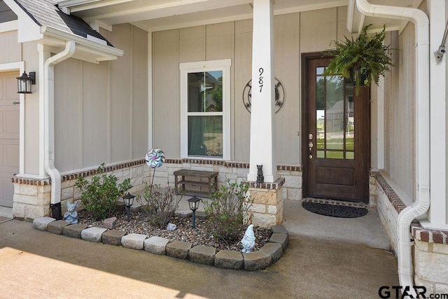 view of exterior entry featuring stone siding, a porch, board and batten siding, and roof with shingles