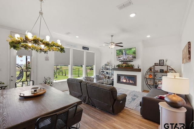 living room with visible vents, a glass covered fireplace, recessed lighting, light wood finished floors, and ceiling fan with notable chandelier