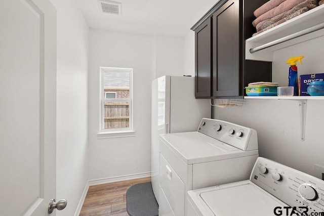 clothes washing area with cabinet space, separate washer and dryer, light wood-type flooring, visible vents, and baseboards