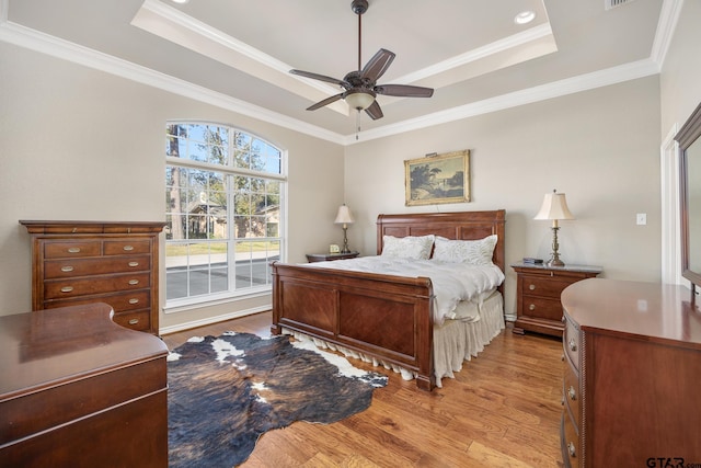 bedroom featuring light hardwood / wood-style floors, crown molding, ceiling fan, and a tray ceiling