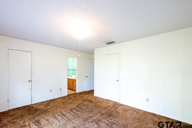 unfurnished bedroom featuring a textured ceiling, visible vents, carpet, and ensuite bath