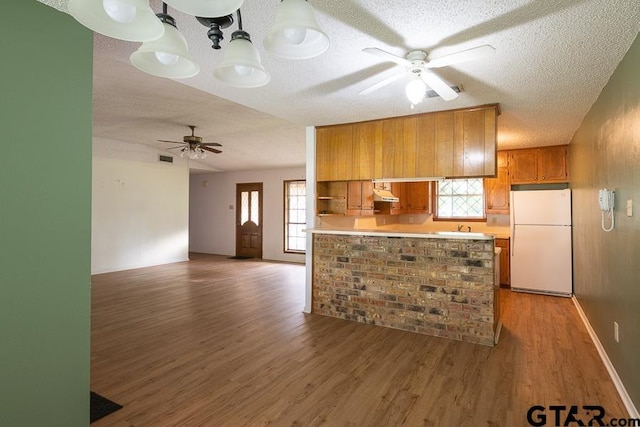 kitchen with freestanding refrigerator, light countertops, brown cabinets, ceiling fan, and light wood finished floors