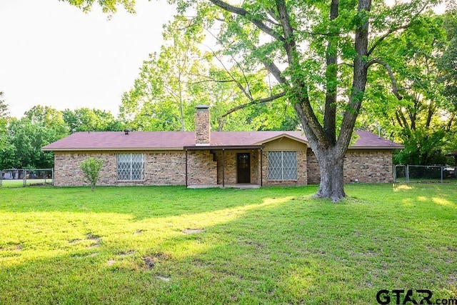 view of front facade featuring a chimney, brick siding, fence, and a front yard