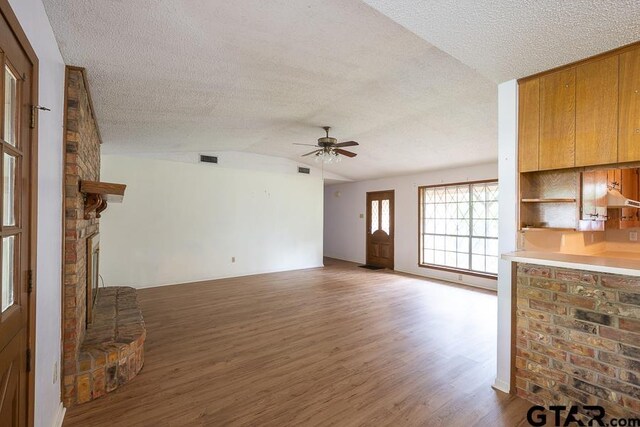 unfurnished living room featuring lofted ceiling, a textured ceiling, visible vents, wood finished floors, and a ceiling fan