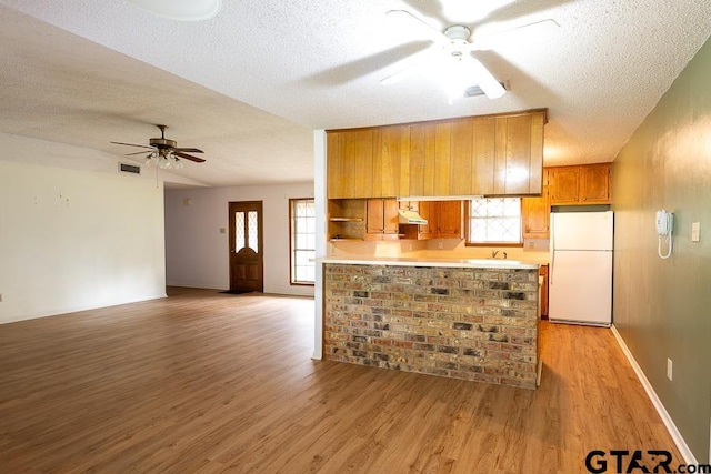 kitchen with brown cabinets, light wood-style floors, ceiling fan, a textured ceiling, and freestanding refrigerator