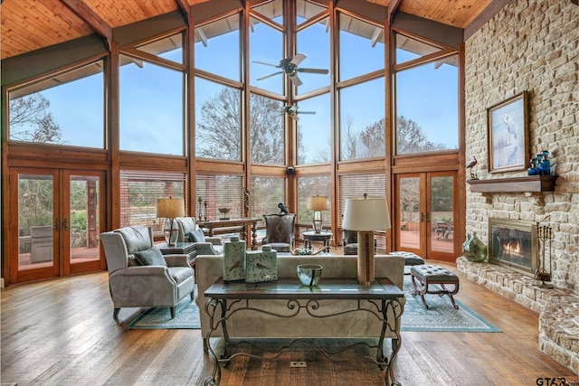 living room with high vaulted ceiling, hardwood / wood-style flooring, a stone fireplace, and french doors