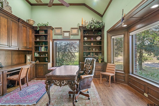 office space featuring ceiling fan, vaulted ceiling, ornamental molding, built in desk, and light hardwood / wood-style flooring