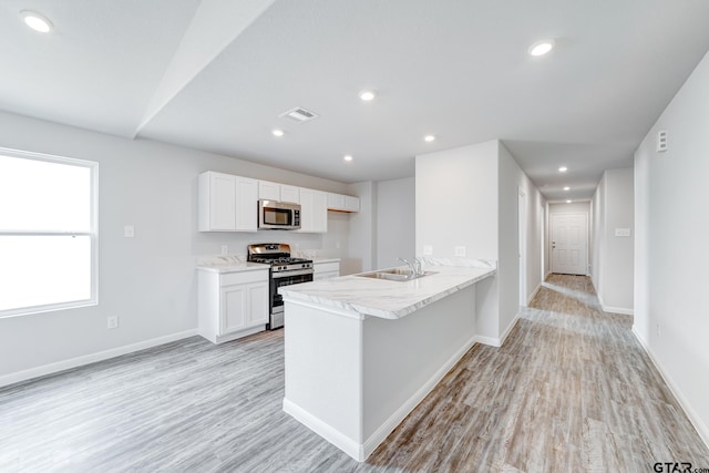 205 Highland Forest Dr, Gilmer, TX 75644 - kitchen featuring appliances with stainless steel finishes, a sink, white cabinetry, light wood finished floors, and a peninsula