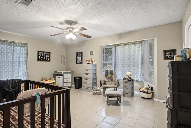 bedroom featuring ceiling fan, light tile patterned floors, a nursery area, and a textured ceiling