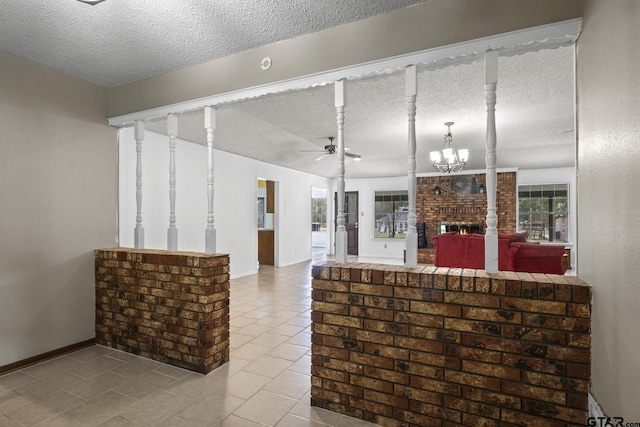 interior space featuring decorative columns, a brick fireplace, and ceiling fan with notable chandelier