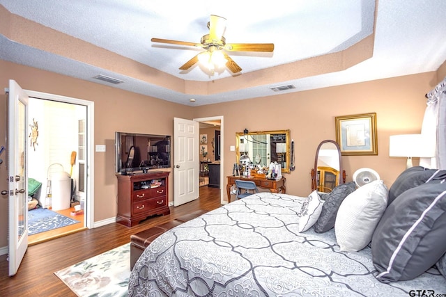 bedroom featuring dark wood-type flooring, a raised ceiling, visible vents, and baseboards