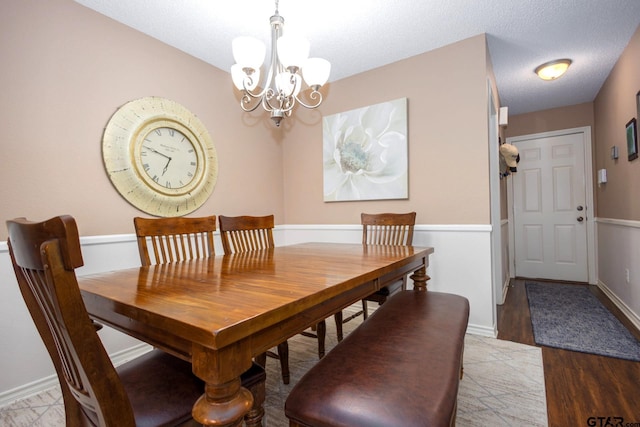 dining room featuring a textured ceiling, baseboards, wood finished floors, and an inviting chandelier