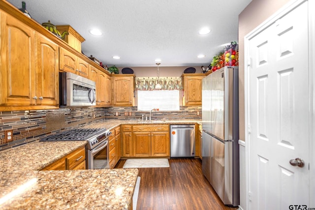 kitchen featuring light stone counters, stainless steel appliances, dark wood-type flooring, a sink, and tasteful backsplash