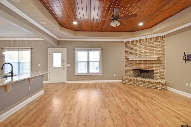 unfurnished living room featuring sink, wood ceiling, light hardwood / wood-style flooring, a tray ceiling, and a brick fireplace