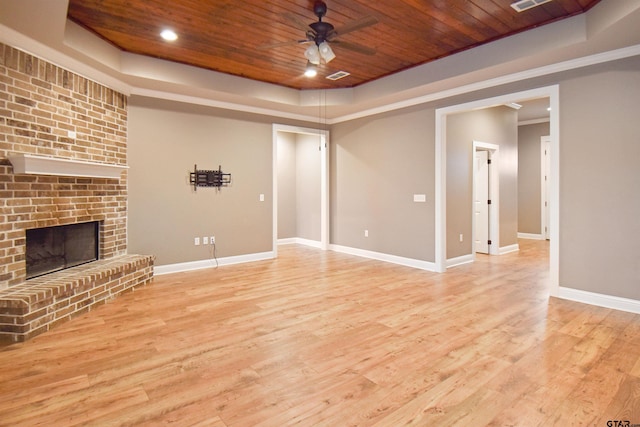 unfurnished living room featuring wood ceiling, a tray ceiling, a brick fireplace, and light wood-type flooring