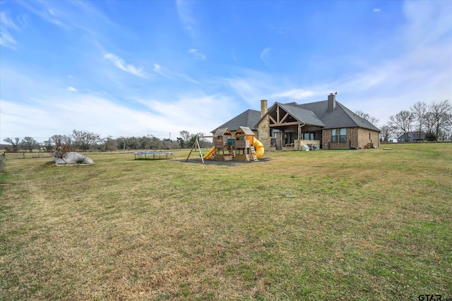 exterior space with a chimney, a playground, a trampoline, a lawn, and brick siding