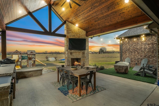 view of patio featuring outdoor dining space, a playground, a grill, and an outdoor stone fireplace