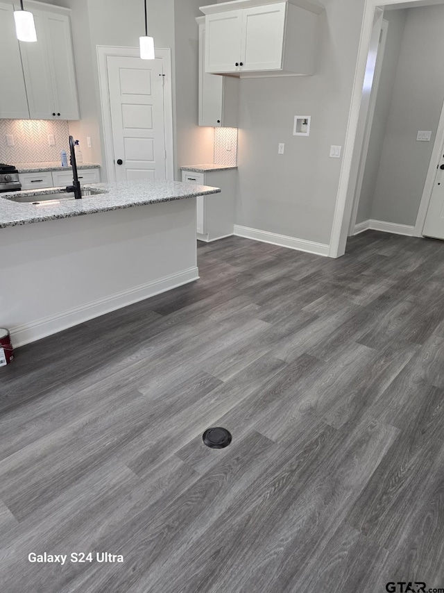 kitchen with white cabinets, light stone counters, a sink, decorative backsplash, and dark wood-type flooring