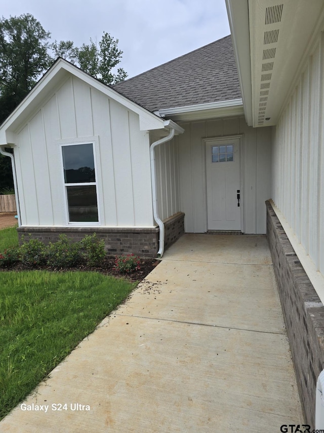 property entrance with board and batten siding, brick siding, a shingled roof, and a lawn