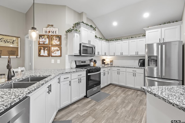 kitchen with lofted ceiling, a sink, stainless steel appliances, white cabinets, and light wood-type flooring