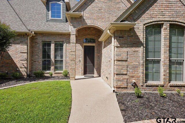 2322 Kingsmill Cir, Tyler, TX 75703 - view of exterior entry featuring a shingled roof, a lawn, and brick siding